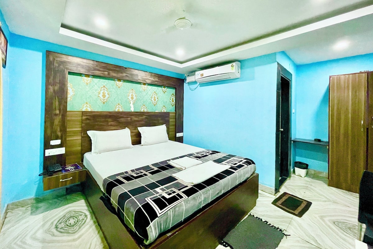 A bedroom with a bed, bedside tables, an air conditioning unit, a wardrobe, and a patterned rug.