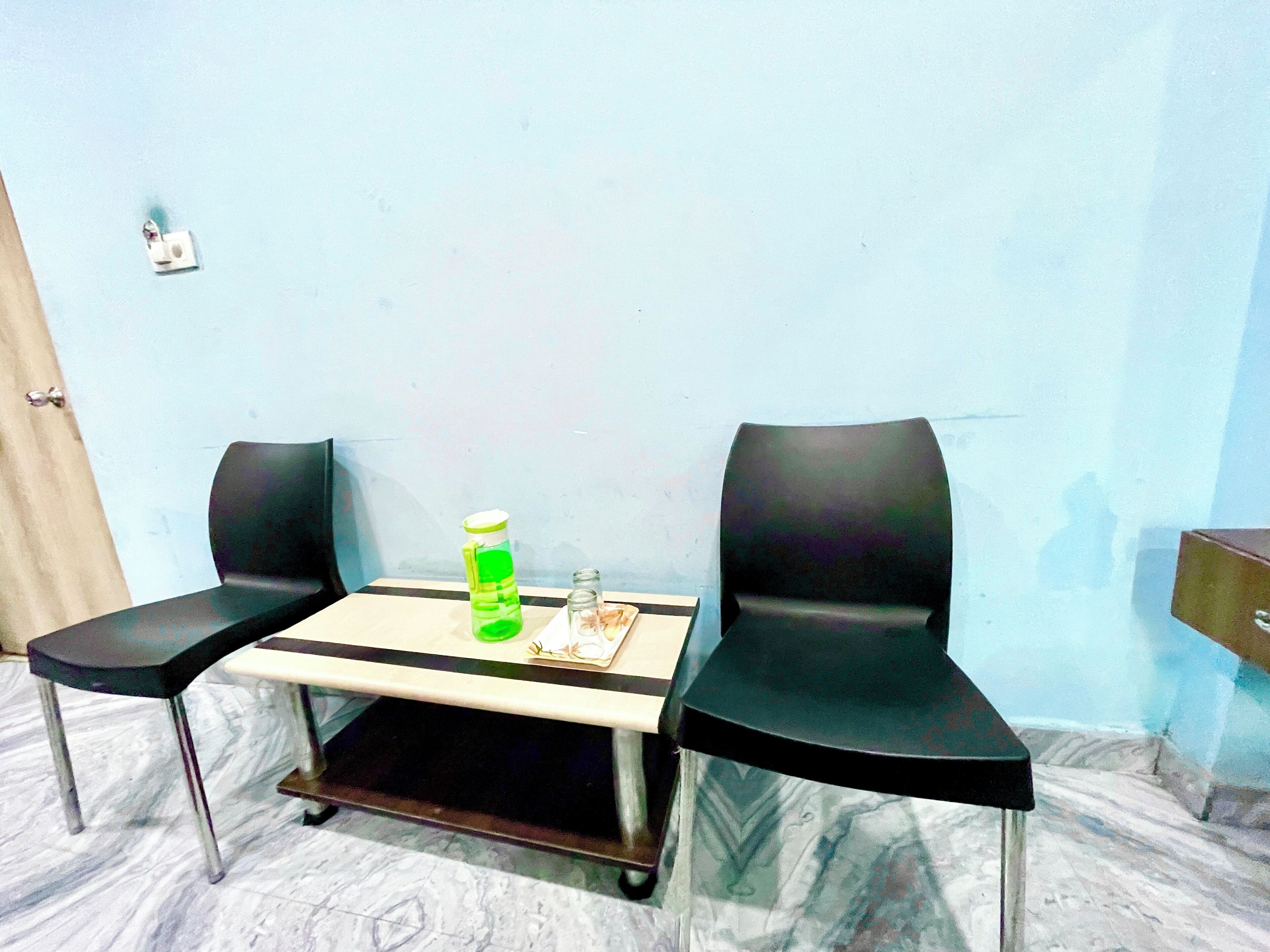 A small room with two black chairs, a table, a green bottle, and a salt shaker.