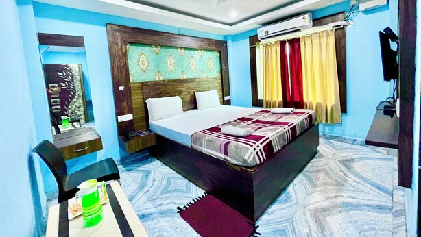 A hotel room with a bed, a desk, a chair, an air conditioning unit, and a television. - Hotel President Inn -near Temple & Beach (Puri)