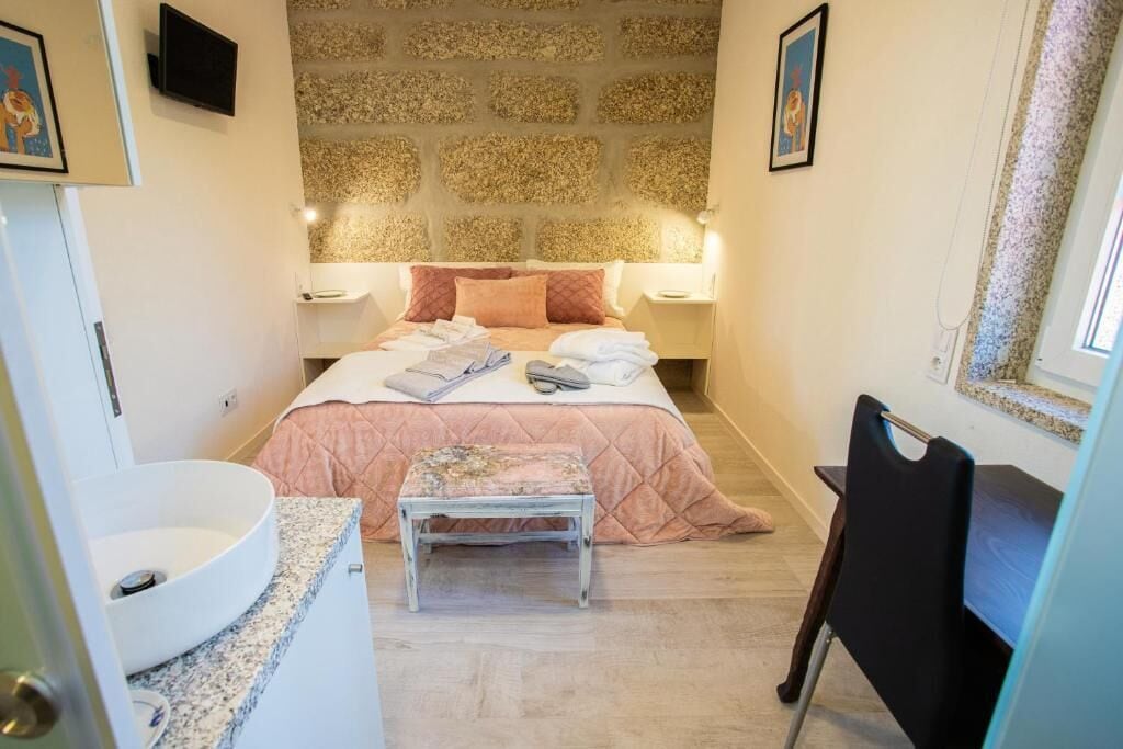 Un dormitorio con cama, mesitas de noche, un taburete pequeño, un escritorio y un televisor instalado en la pared.