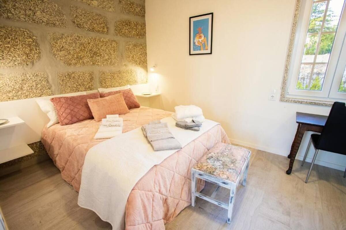 A bedroom with a stone wall, a bed with pink bedding, a small table, and a chair.