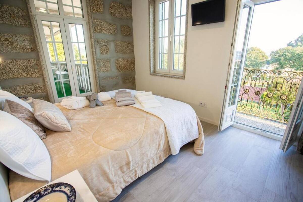 A bedroom with a bed, pillows, a TV, and a balcony with a railing.