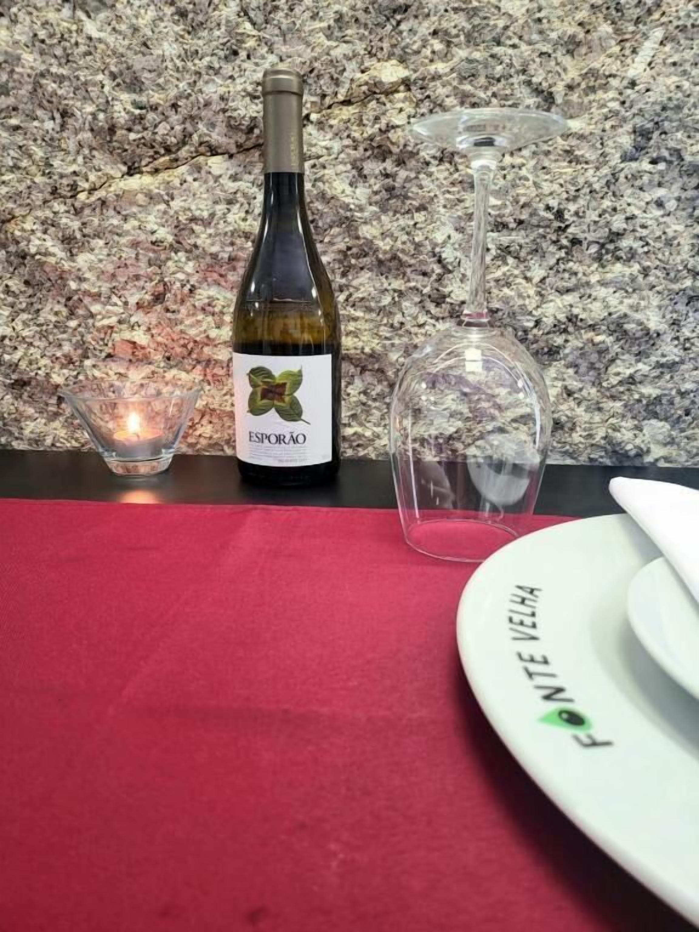 A bottle of wine, a wine glass, a candle, and a plate with the text 'FONTE VELHA' on a table with a red cloth.