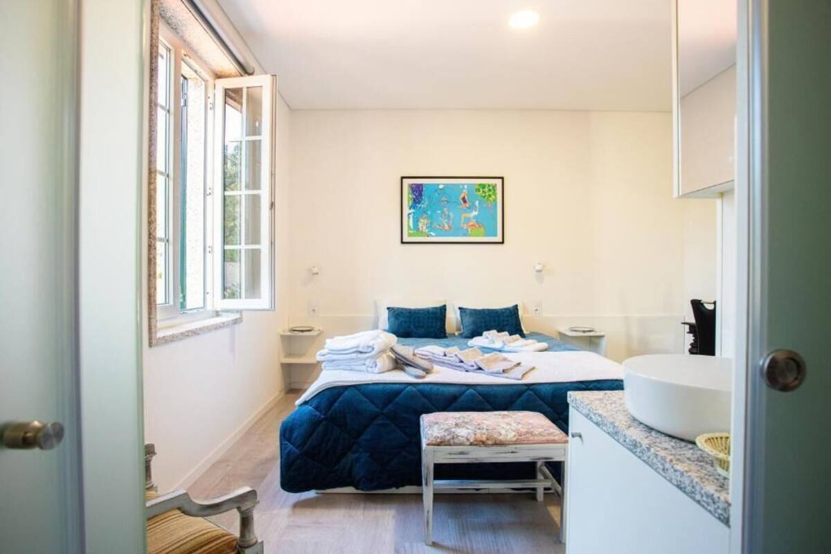 A bedroom with a bed, a bedside table, a bench, a window, and a painting on the wall.