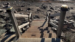 A set of wooden stairs leading to a rocky beach with a clear view of the ocean.