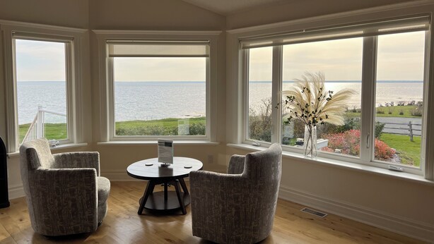 A room with large windows offering a view of the sea, a round table, and two armchairs.