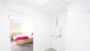 Habitación de hotel moderna con cama, ducha y puerta de baño visible.