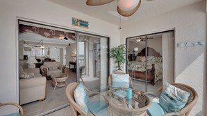 Een ruime woonruimte met een glazen deur naar een slaapkamer, rieten meubilair en een plafondventilator.