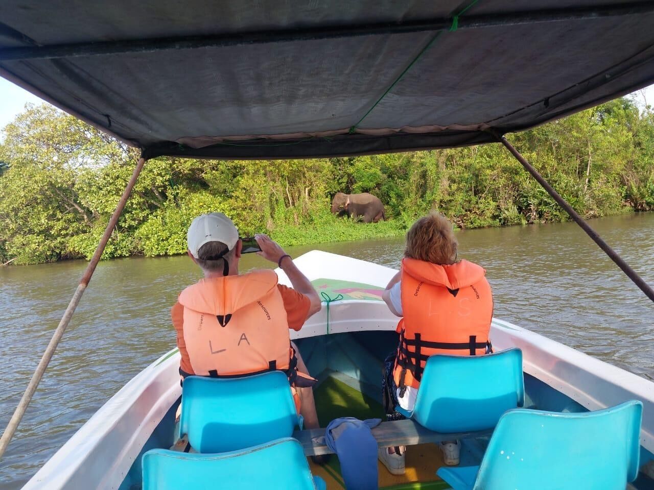 Two people in a boat wearing life jackets, paddling on a calm river surrounded by greenery.