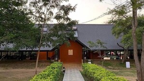 Un edificio tradizionale con tetto in tegole, circondato da vegetazione curata e un vialetto in pietra che conduce all'ingresso.