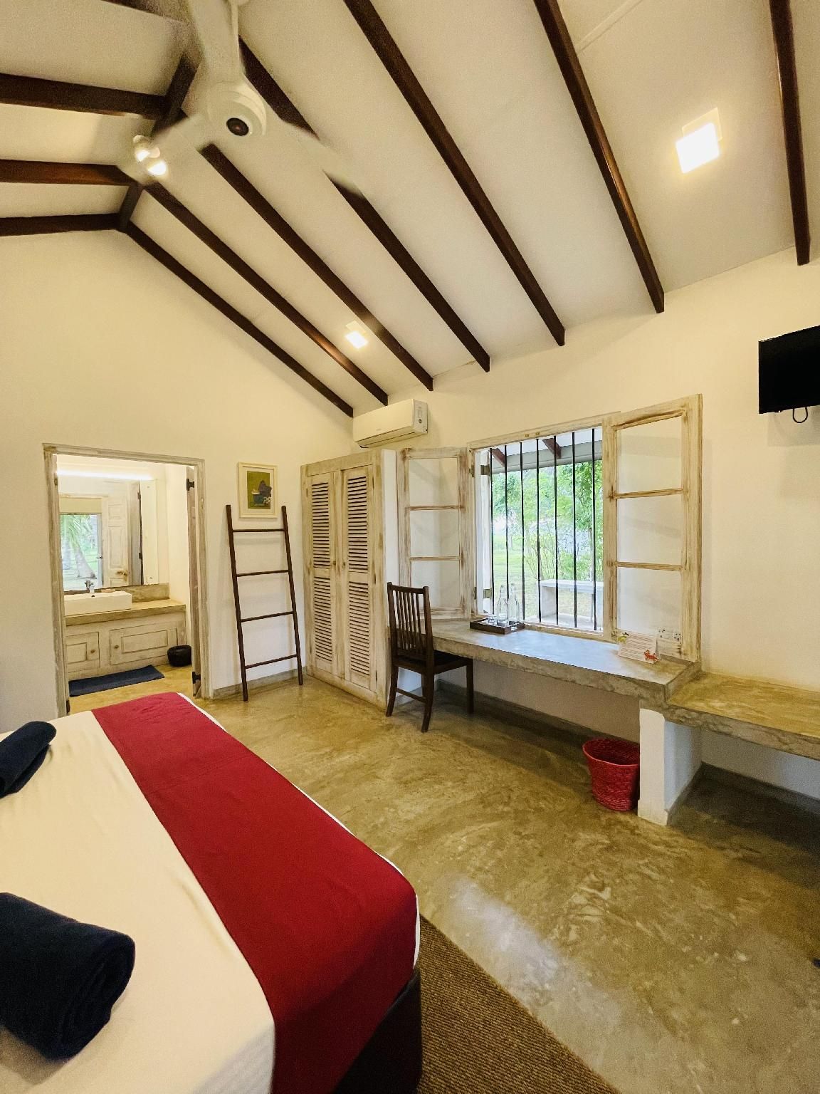 Ein Zimmer mit einem Bett, einem Schreibtisch, einem Stuhl, einem Fenster mit Fensterläden und einem roten Eimer.