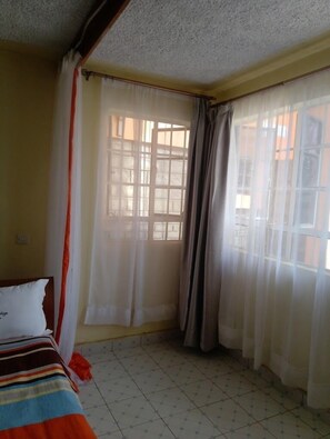 A room with a bed, curtains, and a window. - Kitwe Lodge Oyugis (Oyugis)