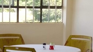 Una stanza con tavoli e sedie rotonde, una finestra vista sul verde e una porta.