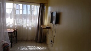 Una stanza con TV a parete, un tavolino e una finestra con tende.
