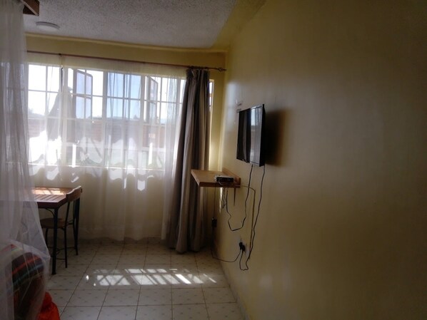 A room with a TV mounted on the wall, a small table, and a window with curtains.