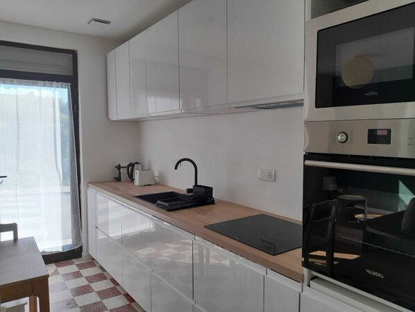 A modern kitchen with white cabinets, a black countertop, a built-in oven, and a window with sheer curtains. - Fisherman's Cabin 300 meters from the beach (Baie de Somme) (AULT)