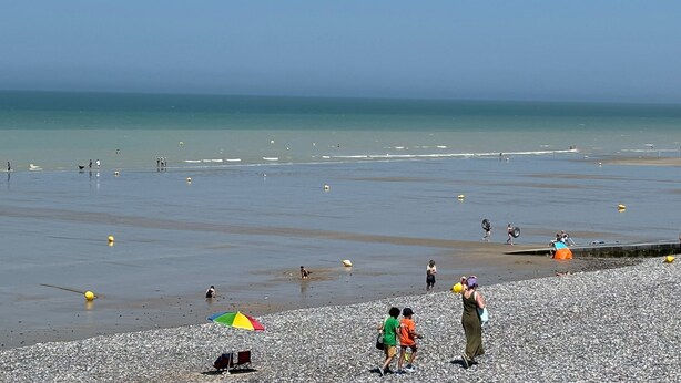Une plage de galets où se trouvent des gens et un parasol coloré.