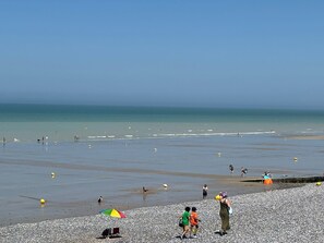 Une plage de galets où se trouvent des gens et un parasol coloré.