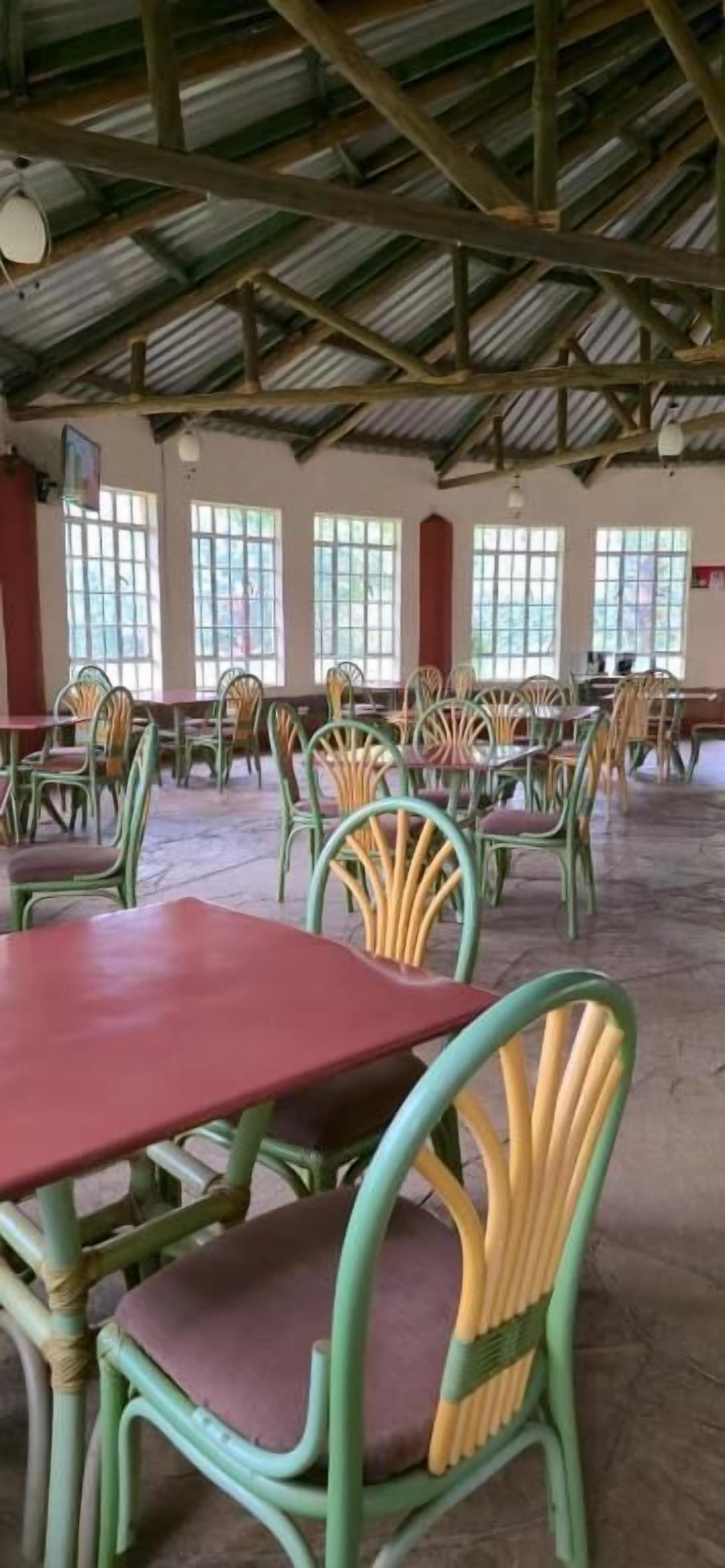 Un comedor amplio con varias mesas y sillas, ventanas grandes y un techo alto con vigas a la vista.