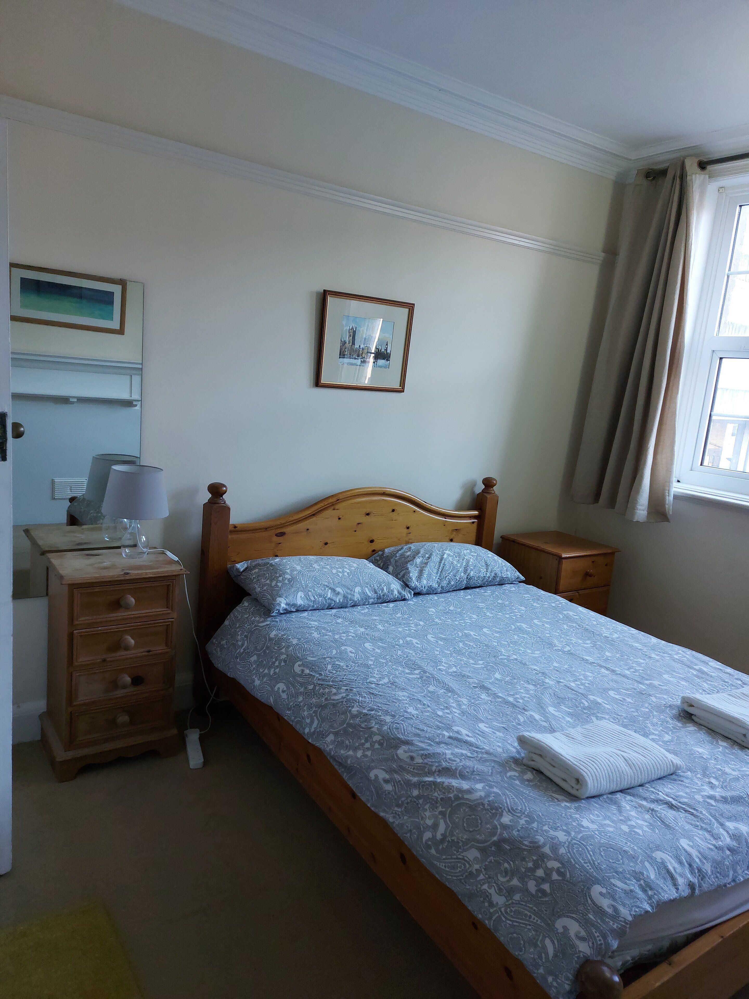 Une chambre à coucher avec un lit en bois, une table de chevet, une lampe, une commode et un tableau encadré au mur.
