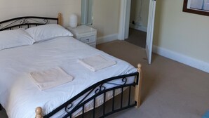 Un dormitorio con cama, mesita de noche, espejo y una puerta que da a otra habitación.