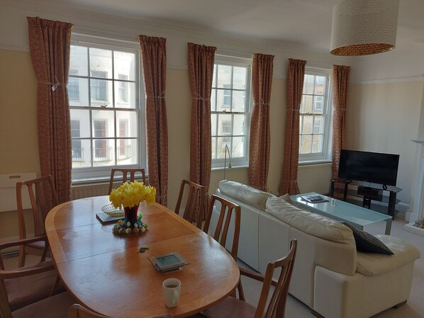 A living room with a wooden dining table, a white sofa, and a TV.