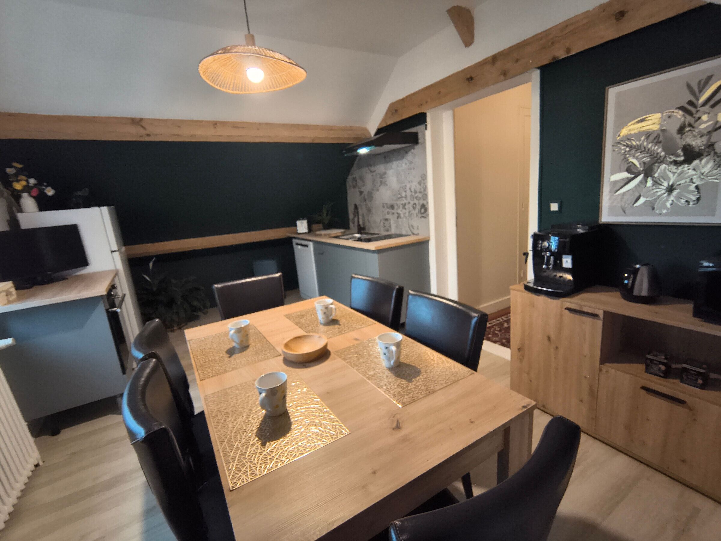 Uma sala de jantar com mesa de madeira, cadeiras, máquina de café e cozinha ao fundo.