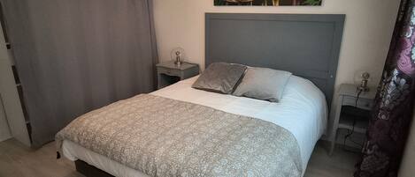 A bedroom with a bed, a nightstand, a lamp, a painting of parrots, and a curtain.