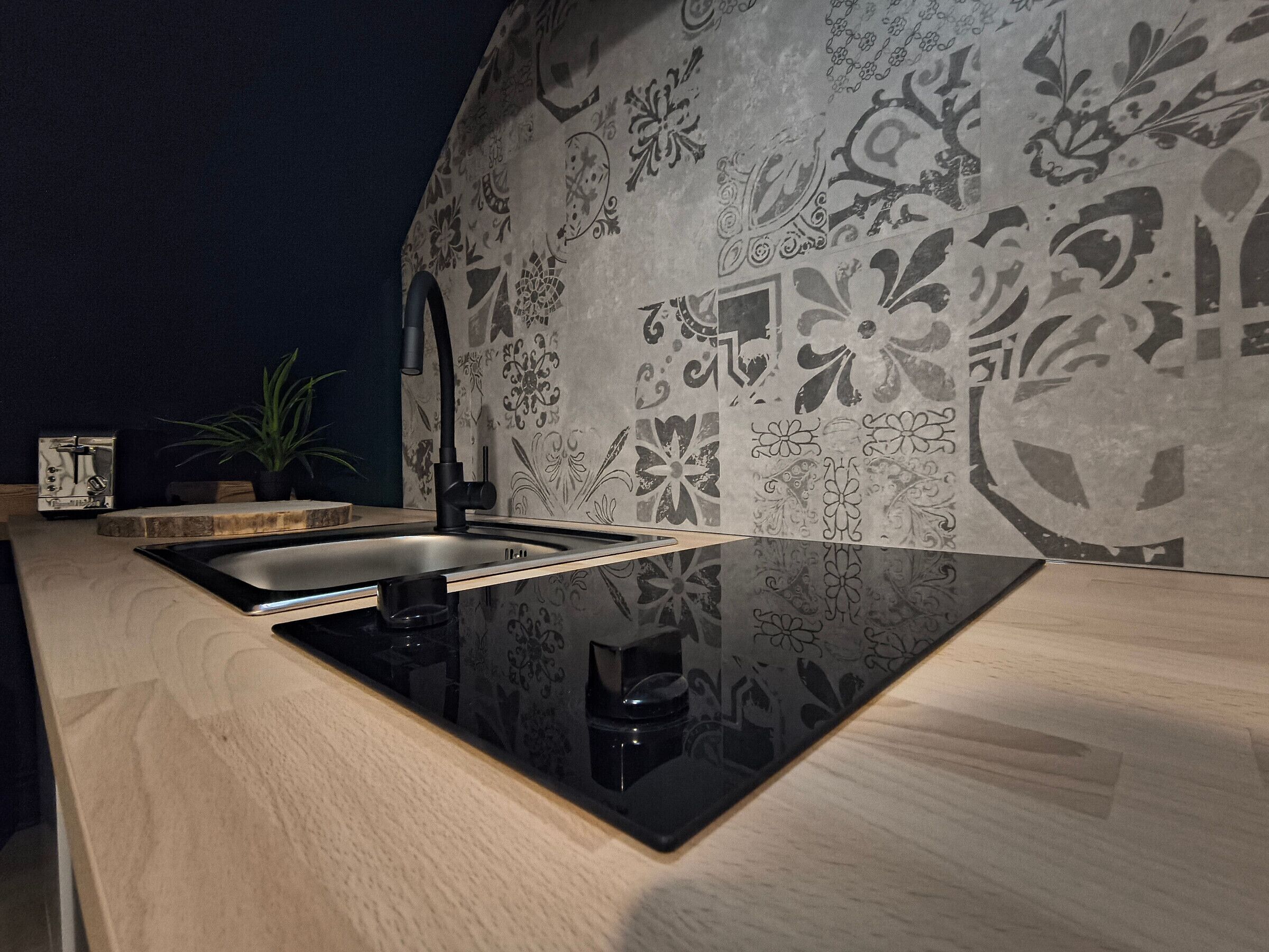 A modern kitchen with a black sink, wooden countertop, and decorative wall tiles.
