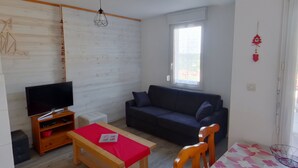 Un salon avec un téléviseur, un canapé, une table en bois et une fenêtre.