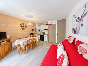 Un salon chaleureux avec un canapé rouge, une table à manger en bois et une cuisine en arrière-plan.