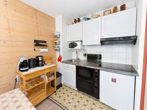 Une cuisine compacte avec des meubles blancs, un four à micro-ondes, un grille-pain et une machine à café.