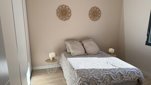 Ein Schlafzimmer mit einem Bett, zwei Wanddekorationen, einem Nachttisch mit Lampe und einem Fenster.