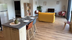 Ein modernes Wohnzimmer mit einer Couch, einem Essbereich mit Tisch für vier Personen und einer Küchenzeile mit Kühlschrank.