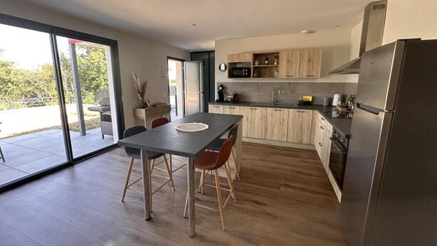 Eine moderne Küche mit Holzschränken, einem Edelstahlkühlschrank und einem Essbereich mit Tisch und Stühlen.