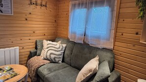 A wooden interior with a sofa, cushions, a table with magazines, and a window with curtains. - Unique Caravan with Private Nordic Bath in La Flèche (La Flèche)