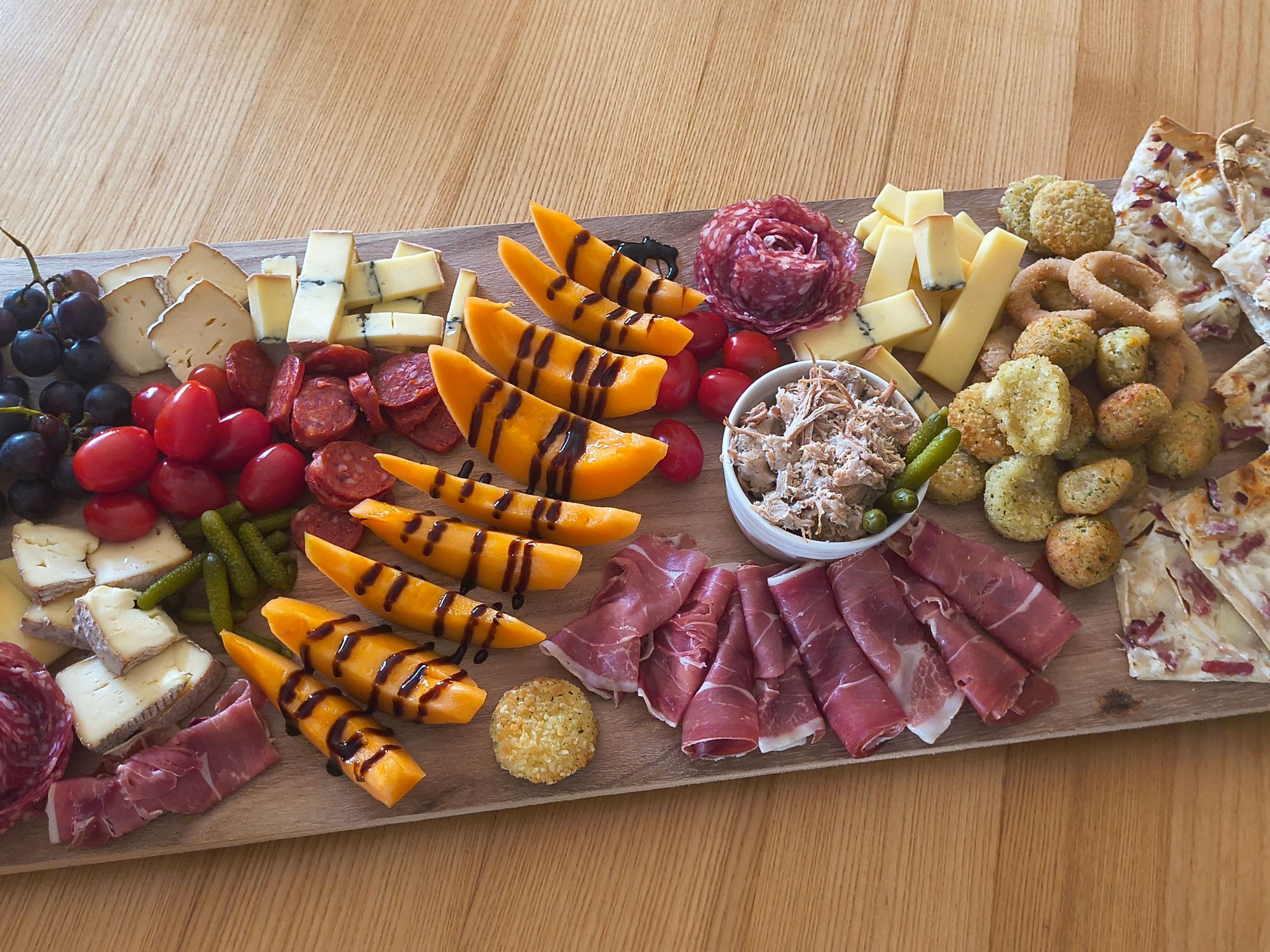 A wooden board with various cheeses, cured meats, and vegetables.