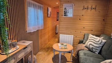 A cozy cabin interior with a wooden wall, a sofa, a small table, and a radiator.