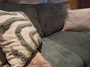 A section of a sofa with a textured cushion and a pillow with a fringe design.