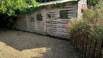 A wooden shed with a corrugated metal roof, surrounded by gravel and greenery.