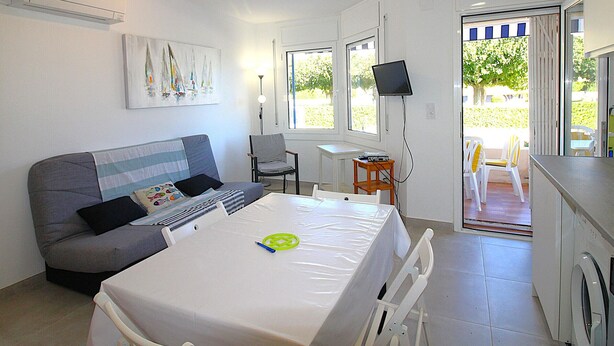 A compact living space with a sofa, a dining table, a TV, and a washing machine. - Renovated apartment 50m from Grifeu Beach (Llançà)