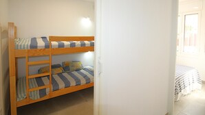 A bunk bed with striped bedding in a room with white walls and a tiled floor. - Renovated apartment 50m from Grifeu Beach (Llançà)