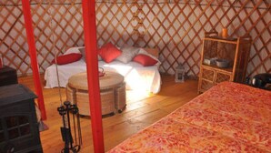 L’intérieur d’une yourte traditionnelle, avec un lit, une petite table et une chaise en osier.