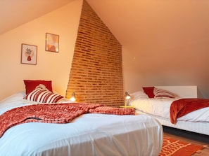 Camera da letto con due letti, parete in mattoni e soffitto spiovente.