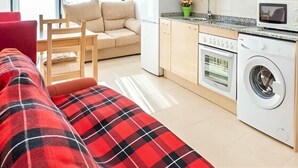 Un apartamento moderno con sofá, una mesa de comedor, una cocina equipada con lavadora y un amplio ventanal.
