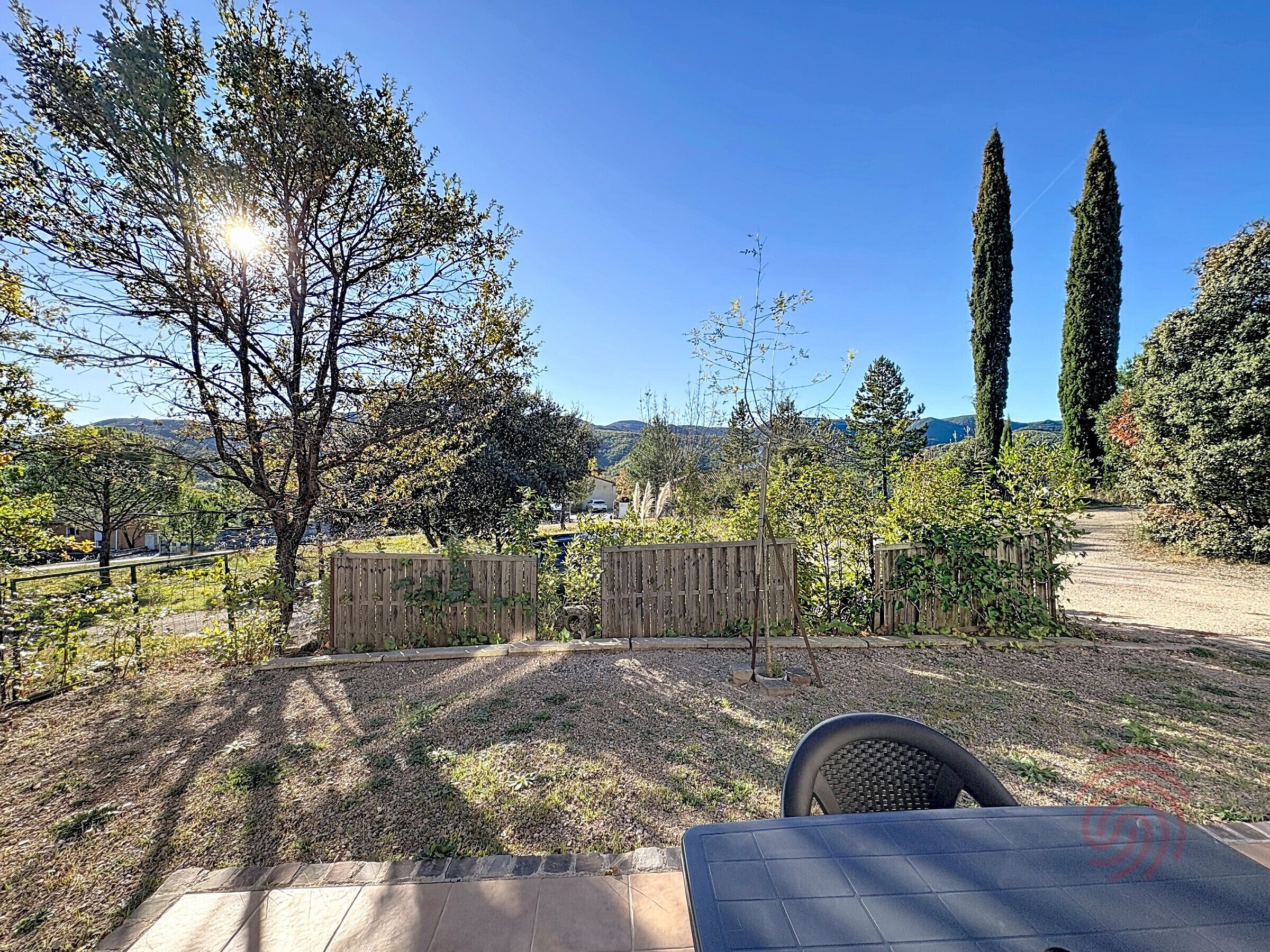 Un jardin avec une terrasse, une clôture en bois et une vue sur des collines lointaines.