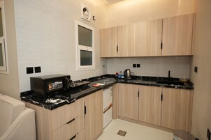 Une cuisine compacte avec des meubles de couleur bois clair, un plan de travail noir et un four à micro-ondes encastré.