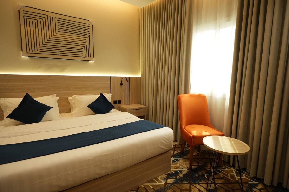 A hotel room with a large bed, a nightstand, a chair, and a small table.
