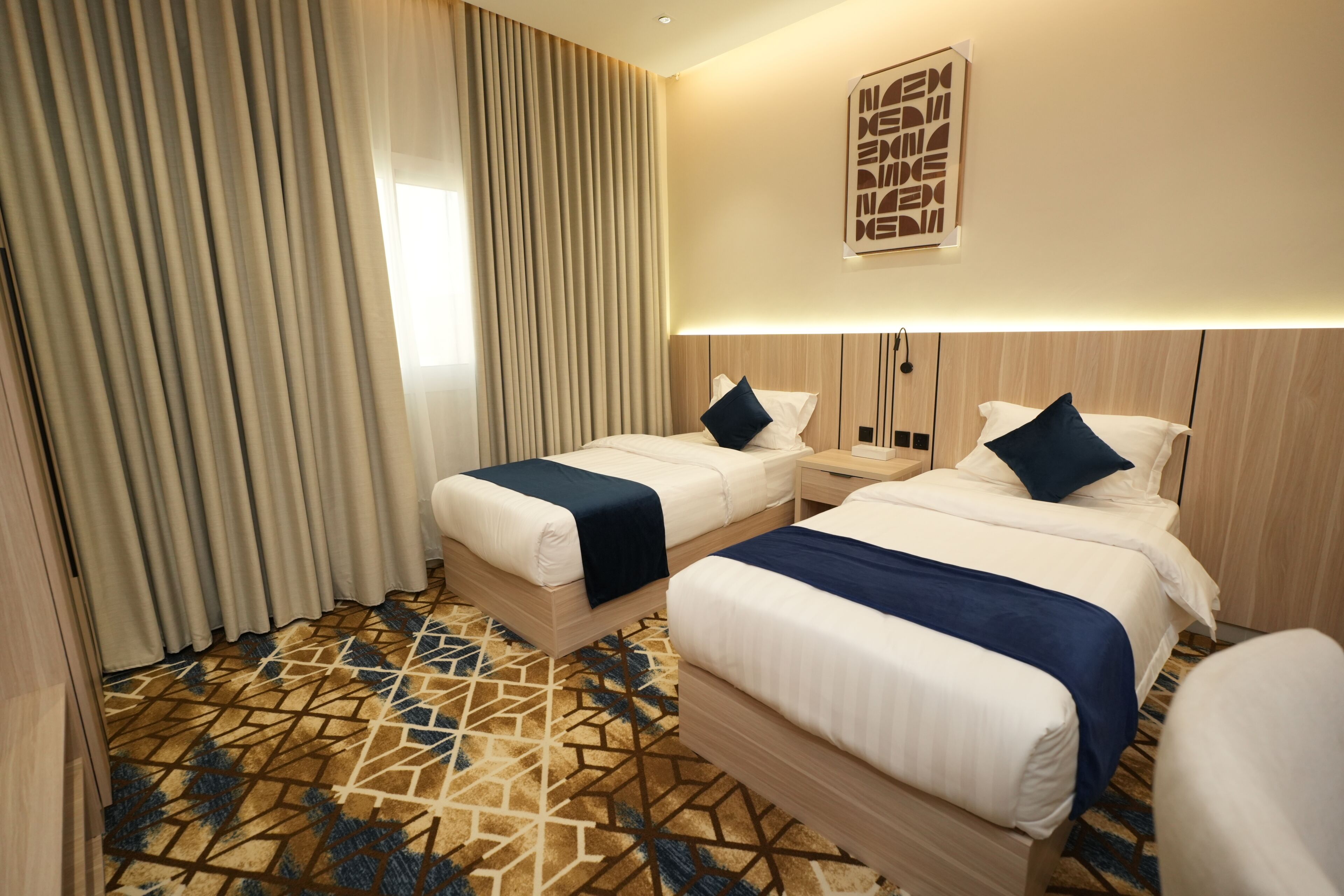 A hotel room with two beds, a patterned carpet, and a large window with curtains.