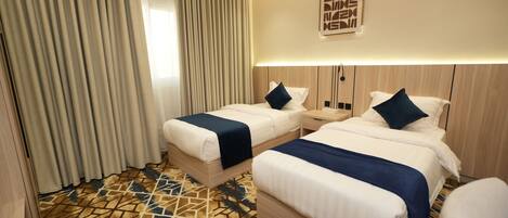 A hotel room with two beds, a patterned carpet, and a large window with curtains.